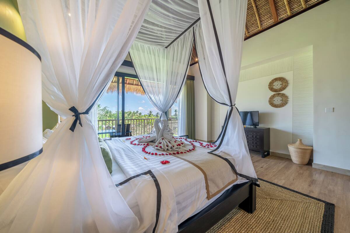 A bed with a canopy, a decorative centerpiece, a television, and a woven basket.