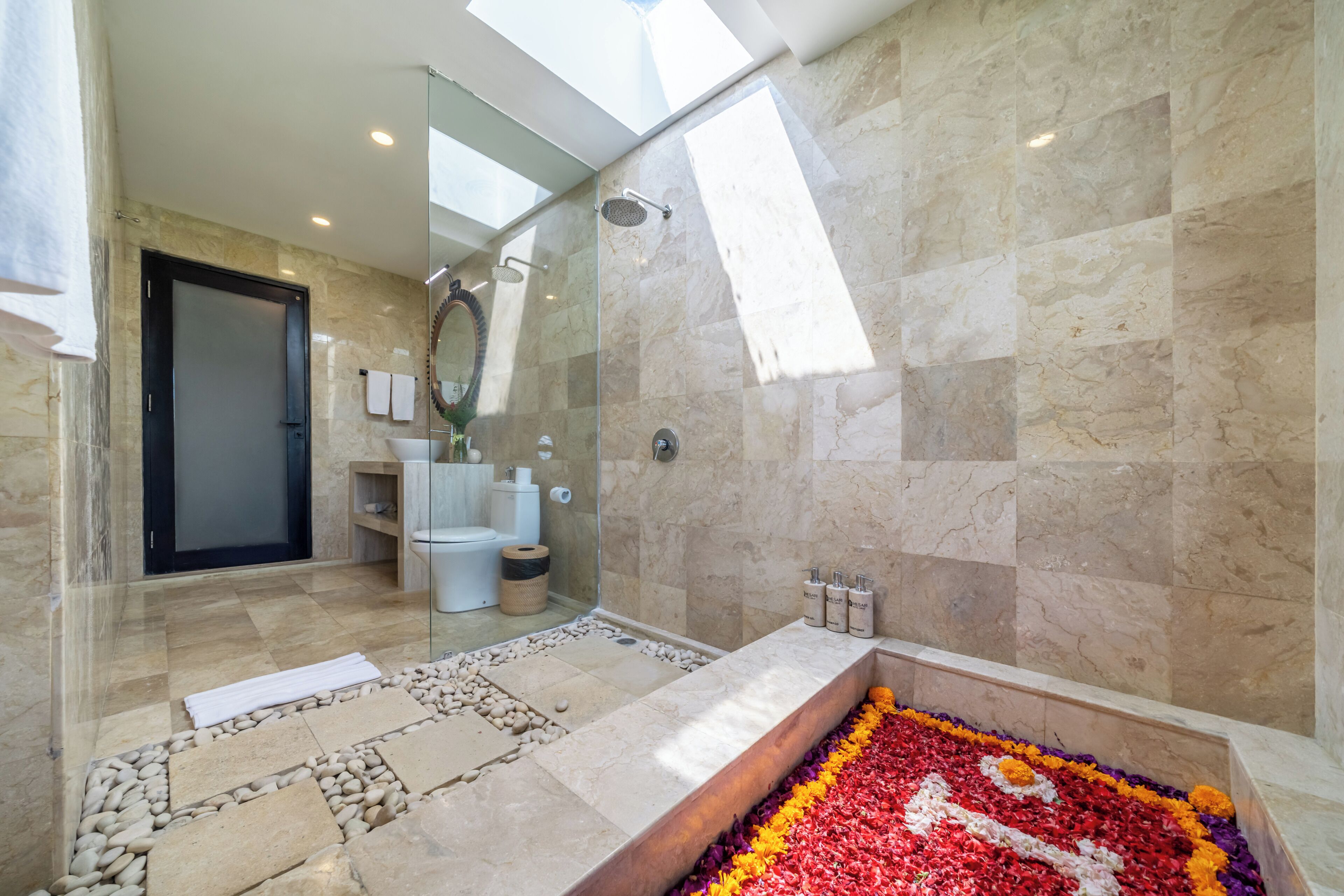 A modern bathroom with a glass shower, marble walls, and a decorative flower arrangement in the bathtub.
