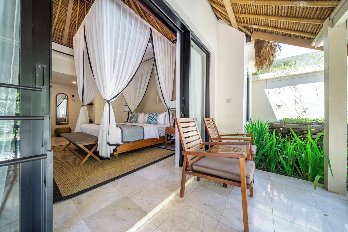 A bedroom with a canopy bed, a wooden chair, and a view of greenery outside.