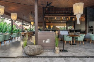 A modern hotel lobby with wooden ceiling, green chairs, a reception desk, and a view of the outdoors.