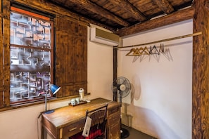 A room with a wooden desk, a chair, a window with a geometric pattern, an air conditioner, a fan, and a clothes drying rack. - Li river retreat house Laojia  (Guilin)