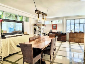A spacious dining area with a wooden table and wicker chairs, a bookshelf, and a vintage typewriter on a desk.