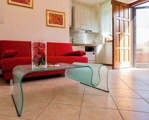 Ein modernes Wohnzimmer mit einem roten Sofa, einem Glastisch und einer Küche im Hintergrund.