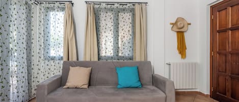 Ein Wohnzimmer mit grauem Sofa, beigen und blauen Kissen, einer Holztür und gemusterten Vorhängen.