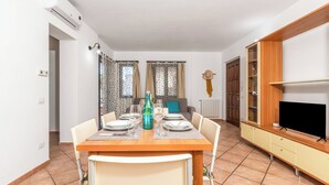 Een eetgedeelte met een tafel voor vier personen, een televisie op een houten standaard en een garderobe met spiegel.