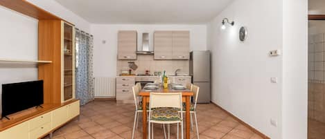 Una cocina compacta con área de comedor, un televisor sobre un soporte de madera y piso de baldosas.