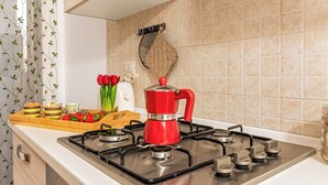 Een keuken met een gasfornuis, een rode waterkoker, een dienblad met etenswaren en een houten snijplank.