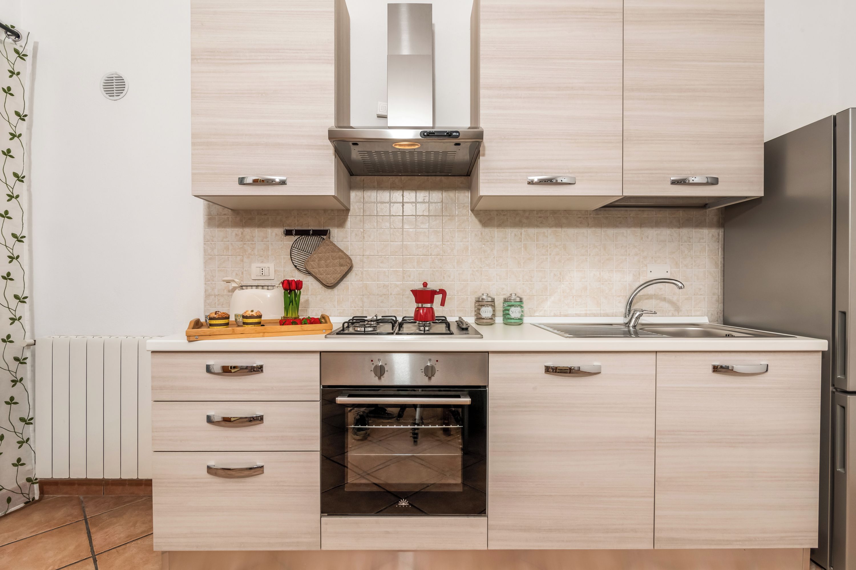 Een moderne keuken met licht houten keukenkastjes, een roestvrijstalen afzuigkap, een inbouwoven en een roestvrijstalen koelkast.