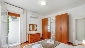 A bedroom with a bed, wooden wardrobe, a mirror, and a door leading to a balcony.