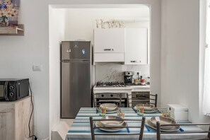 A kitchen with a refrigerator, stove, microwave, and dining table set with plates and cups. - Casa Tolly Rapallo (Rapallo)