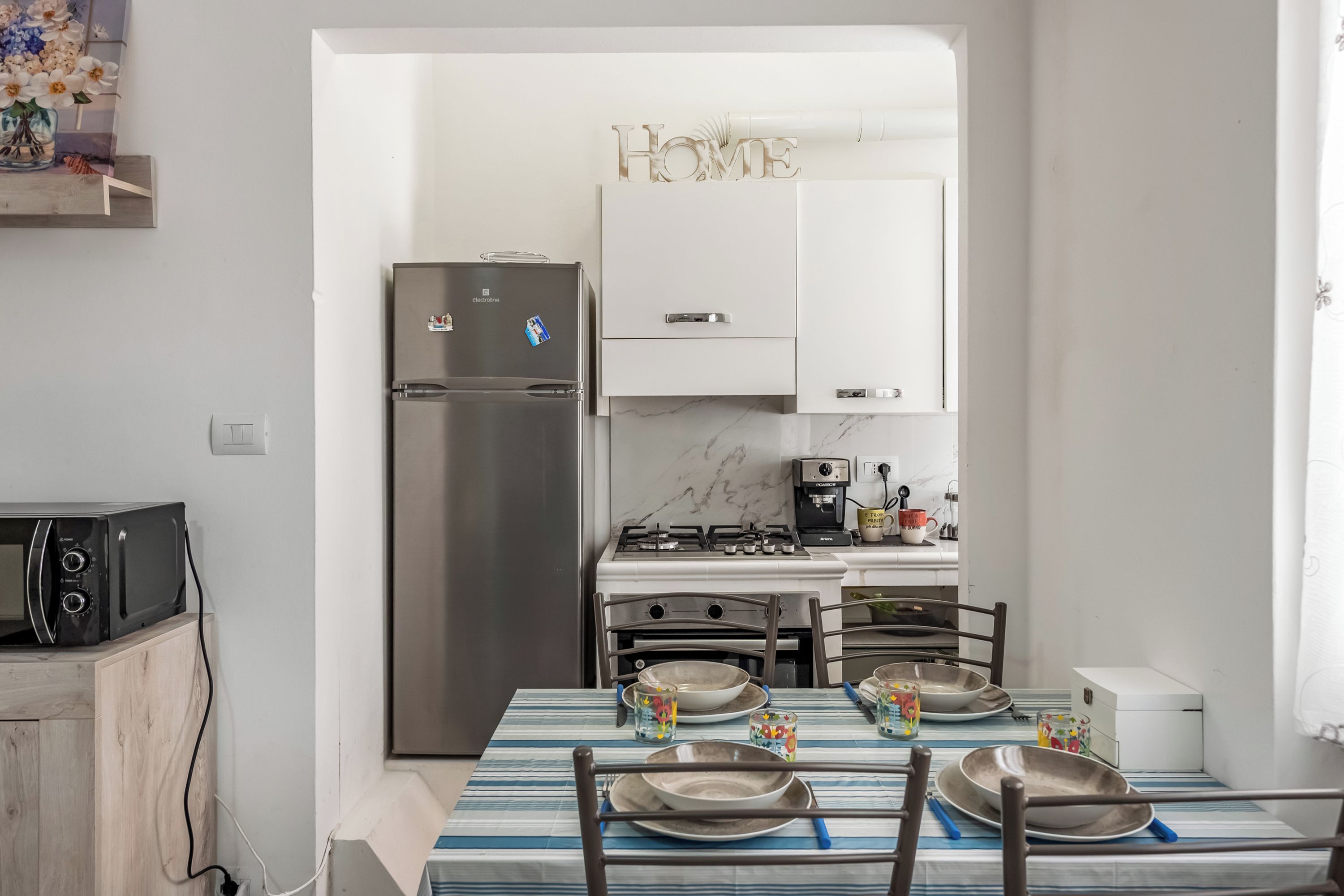 Cozinha equipada com geladeira, fogão, micro-ondas e mesa de jantar posta com pratos e xícaras.