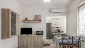 A compact kitchen with a microwave, stove, and refrigerator. There is a dining table with chairs and a TV on a wooden cabinet.
