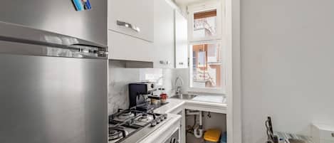 Una cocina compacta con un refrigerador de acero inoxidable, una estufa a gas y muebles de color blanco.