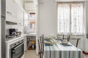 A kitchen with white cabinets, a stove, and a dining table set with plates and bowls. - Casa Tolly Rapallo (Rapallo)