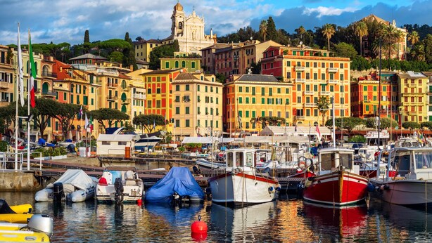 A marina with boats docked, surrounded by colorful buildings and a prominent church in the background.