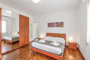 A bedroom with a wooden bed, a nightstand with a lamp, a mirror, and a painting on the wall. - Casa Tolly Rapallo (Rapallo)