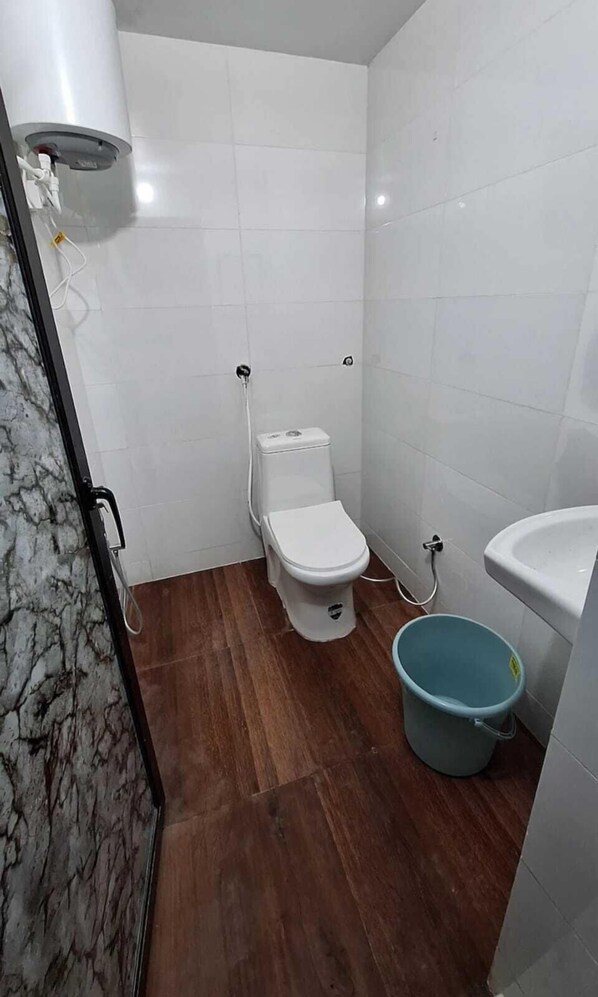 A small bathroom with a toilet, a shower, a sink, and a bucket. - HOTEL WHITE PALACE (Nawa)