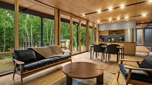 A modern interior with a sofa, round table, and dining area, large windows with a forest view. - 3 Luxury Cabins on 40 wooded acres @ Oak & Ember Luxury Resort (Wisconsin Dells)
