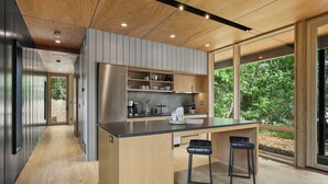 A modern kitchen with a central island, bar stools, and large windows offering a view of greenery. - 3 Luxury Cabins on 40 wooded acres @ Oak & Ember Luxury Resort (Wisconsin Dells)
