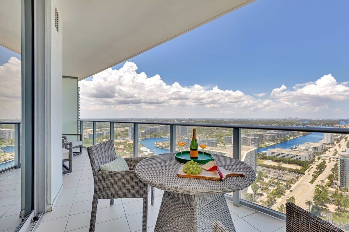 Ein Balkon mit Korbmöbeln, einem Tisch mit Flasche, Gläsern und einer Obstplatte.