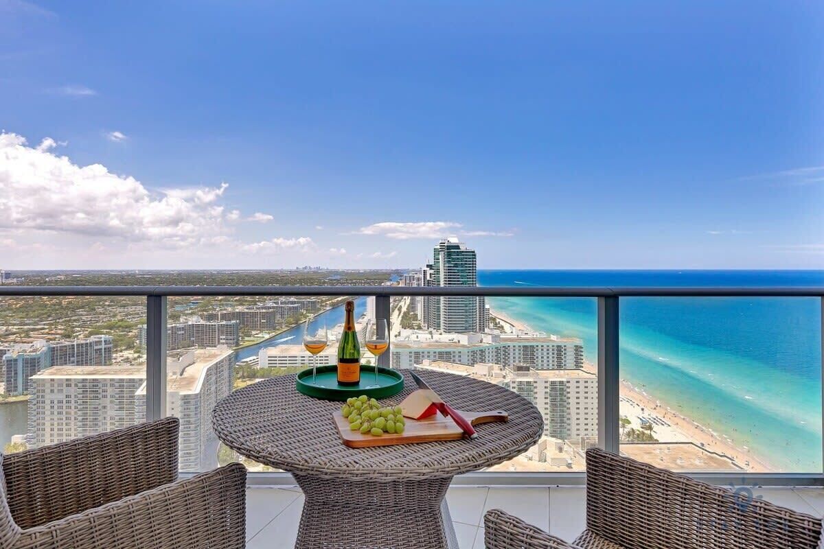 A balcony with wicker furniture, a bottle of wine, and a fruit platter.