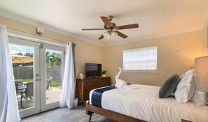 Ein Schlafzimmer mit einem Bett, einem Deckenventilator, einem Fernseher auf einer Holzkommode und einer Schiebetür, die auf eine Außenpatio führt.