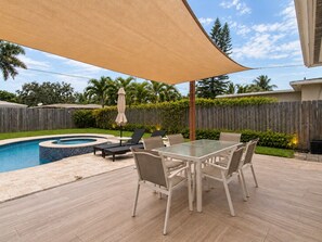 Ein Garten mit Swimmingpool, überdachter Terrasse und Liegestühlen.