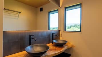 A modern bathroom with two large bowls as sinks, a wooden countertop, a mirror, and a view of greenery through the windows.