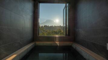 A modern bathroom with a large window, dark tiled walls, and a reflective floor.