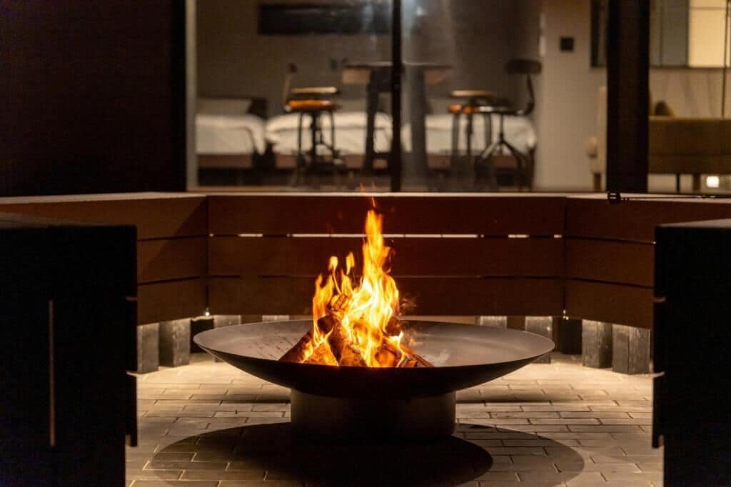 Una chimenea con un banco al frente, una cama al fondo y un comedor con mesas y sillas.