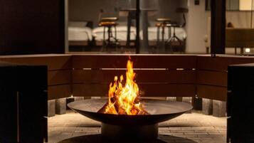 Una chimenea con un banco al frente, una cama al fondo y un comedor con mesas y sillas.