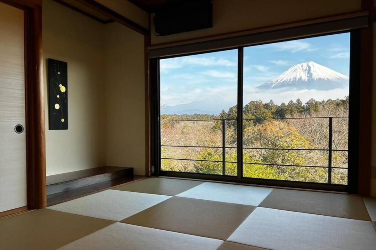 A room with tatami flooring, a sliding door, and a large window with a view of a mountain.