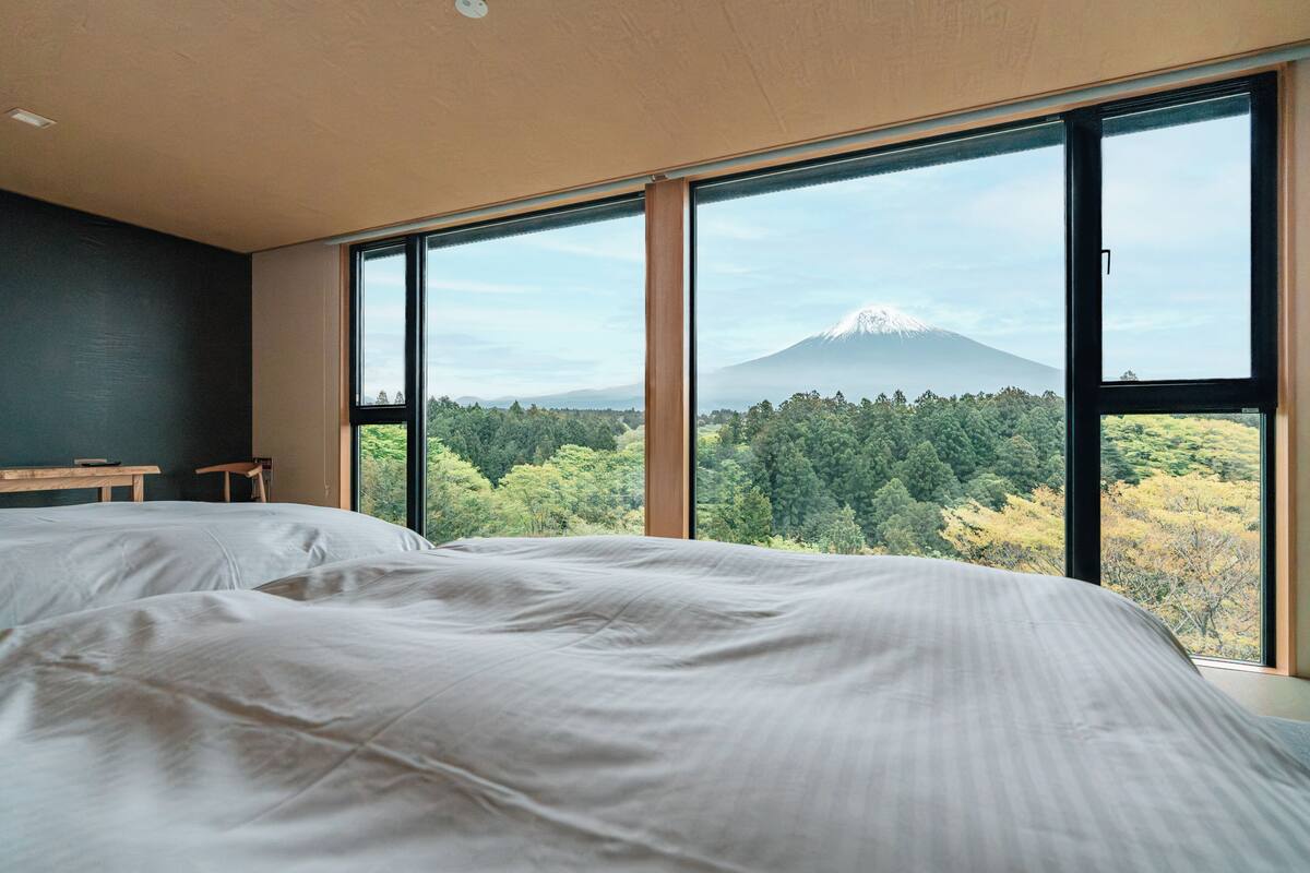 A bedroom with a large window, a bed, a bench, and a desk.