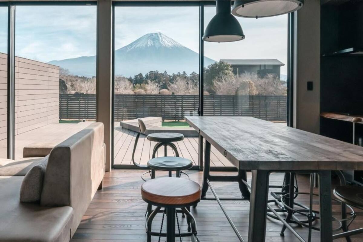 A modern interior with a wooden deck, a dining table, and bar stools. A large window offers a view of a mountain.