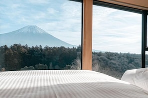 A bed with a view of a mountain through a window.