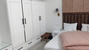 A bedroom with a bed, white wardrobe, bedside table, and a wall-mounted lamp. - Tranquil Nature Resort (Dehradun)