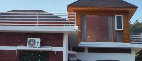 A two-story building with a flat roof, a balcony, and a large window on the upper floor.