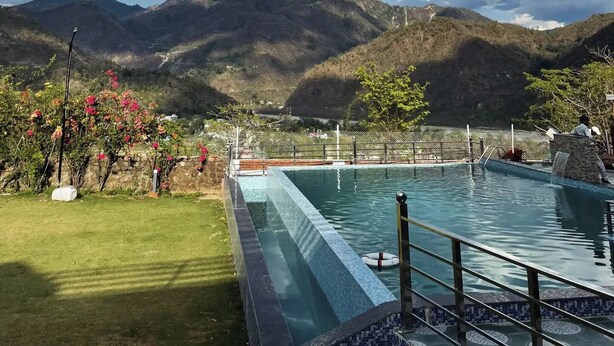 A swimming pool with a view of mountains, a grassy area, and a fence. - Tranquil Nature Resort (Dehradun)