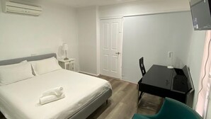 Una habitación de hotel con cama, escritorio, silla, televisión y aire acondicionado.