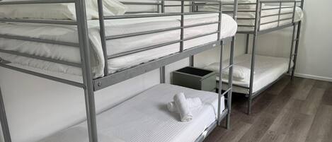 Dormitorio con literas de metal, ropa de cama blanca y una mesita de noche pequeña verde.