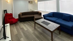 Una sala moderna con un sofá marrón, un sofá azul, un sillón de peluche rojo, una mesa de centro y un televisor sobre un mueble.