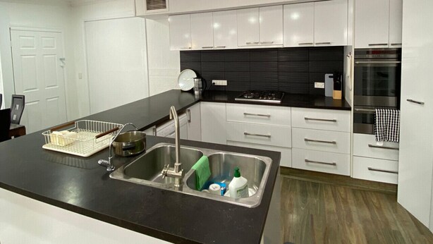 Una cocina moderna con armarios blancos, encimera negra y electrodomésticos de acero inoxidable.