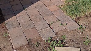 Un espacio al aire libre techado con un sendero pavimentado, una silla y un edificio con amplias ventanas.