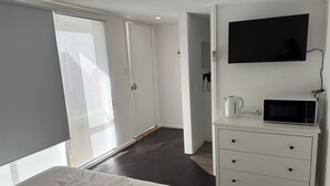 Habitación de hotel con una cama, televisor, microondas y cómoda blanca.