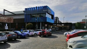 Un estacionamiento con varios coches, un edificio de fachada azul y un cartel que dice 'Pacific Toys'.