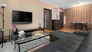 Un salon avec un téléviseur, un canapé, une table basse en verre et un mur en briques.