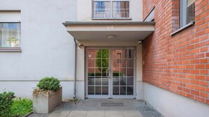 Une entrée d’immeuble avec une porte en verre, un petit bac à fleurs contenant une plante et une enseigne au-dessus de la porte.