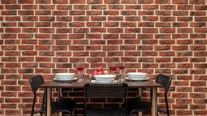 Un mur de briques avec une table dressée pour le repas, comprenant des assiettes, des verres et des fruits.