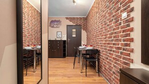 Un couloir aux murs de briques, avec un plancher en bois, un coin repas comprenant des chaises et des tables, et une porte donnant sur une autre pièce.