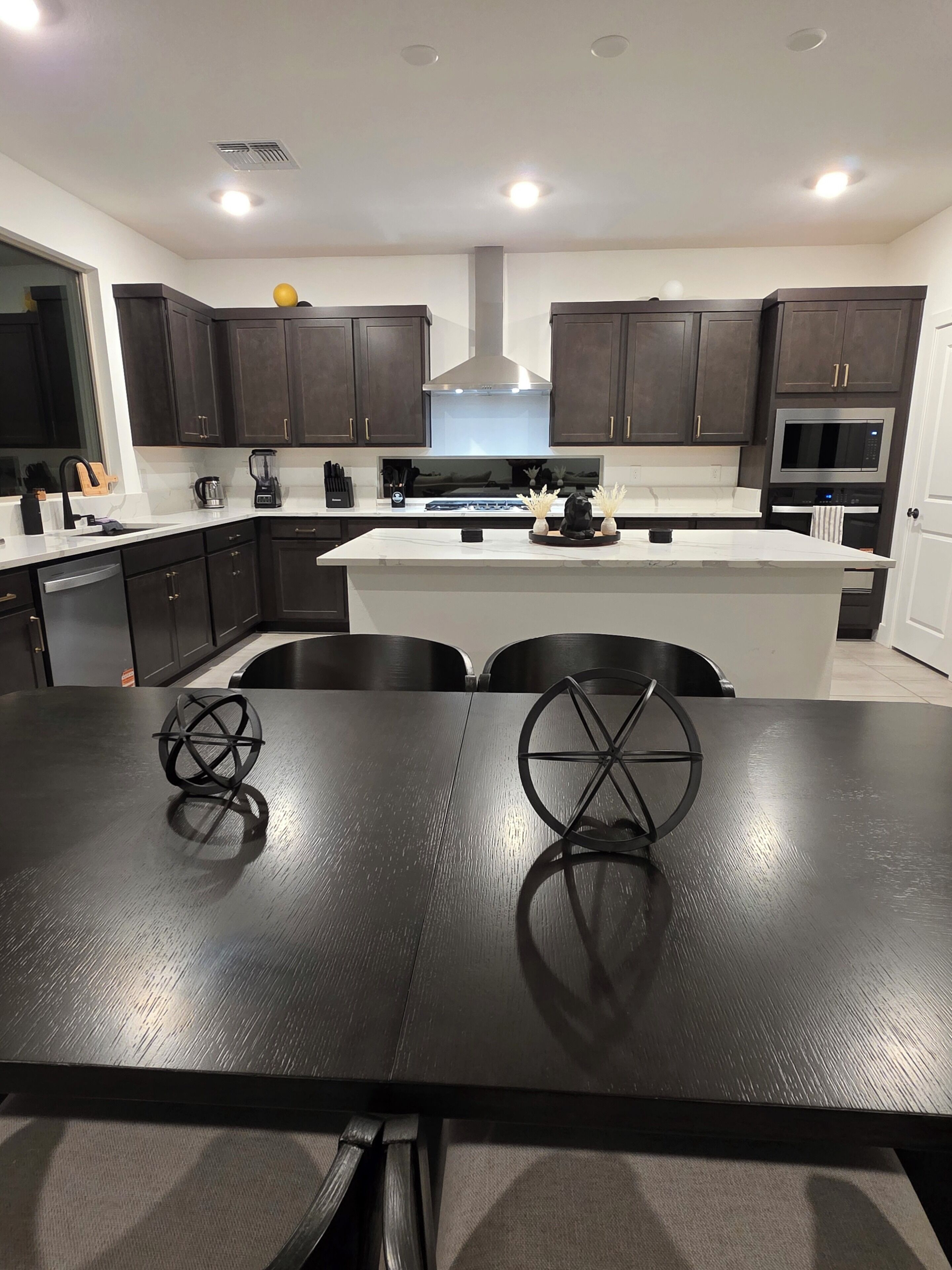Uma cozinha moderna com armários escuros, uma ilha central e uma mesa de jantar com cadeiras.
